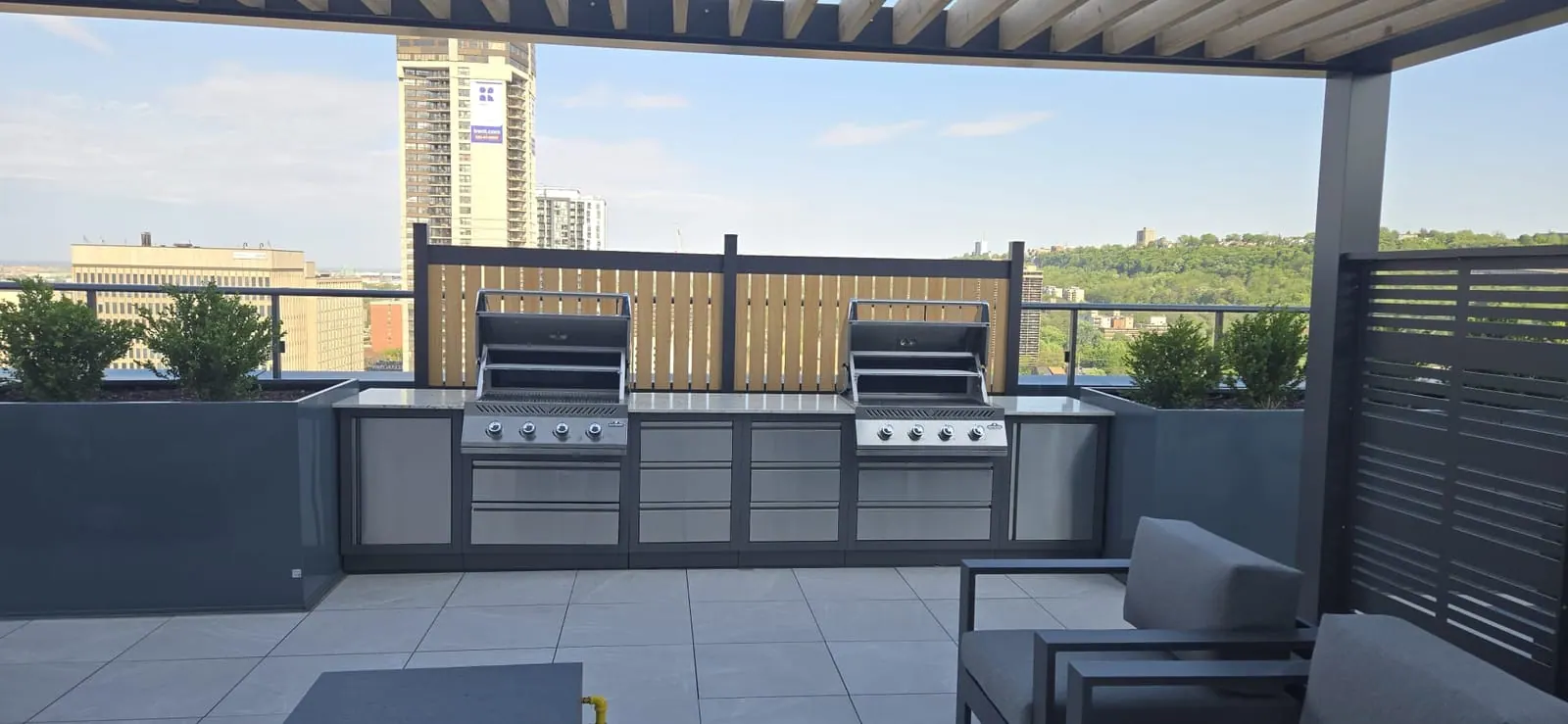 Two large barbecue grills set into a sleek outdoor kitchen on the rooftop, a downtown tower in the distance.