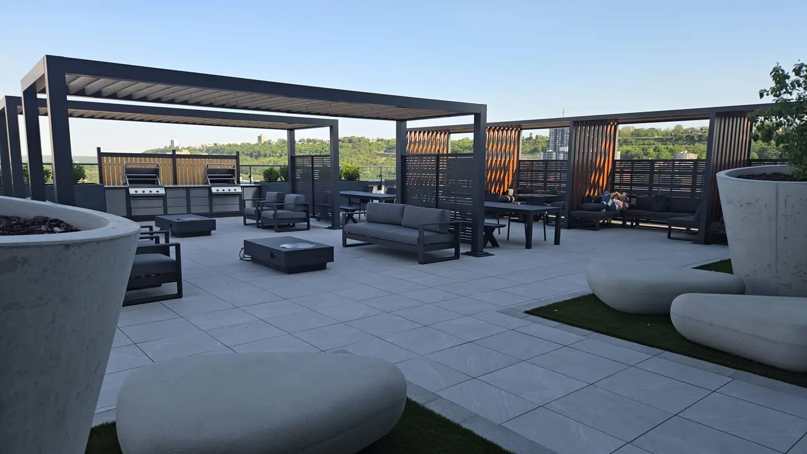 Rooftop terrace at dusk with modular sofas, a fire-pit table and gas grills under a pergola.