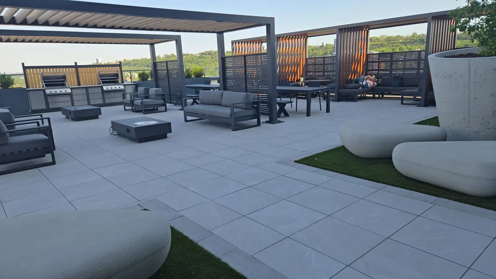 Overview of the rooftop terrace: grill station, pergola lounges, a fire-pit table and sculptural benches.