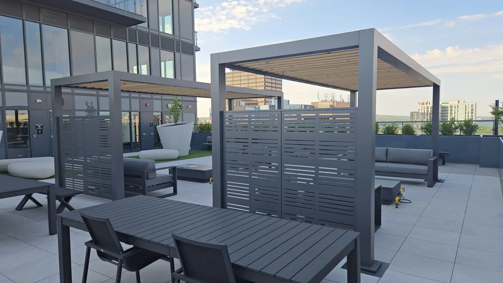 Modern grey pergolas with slatted screens over outdoor dining tables on the rooftop terrace.