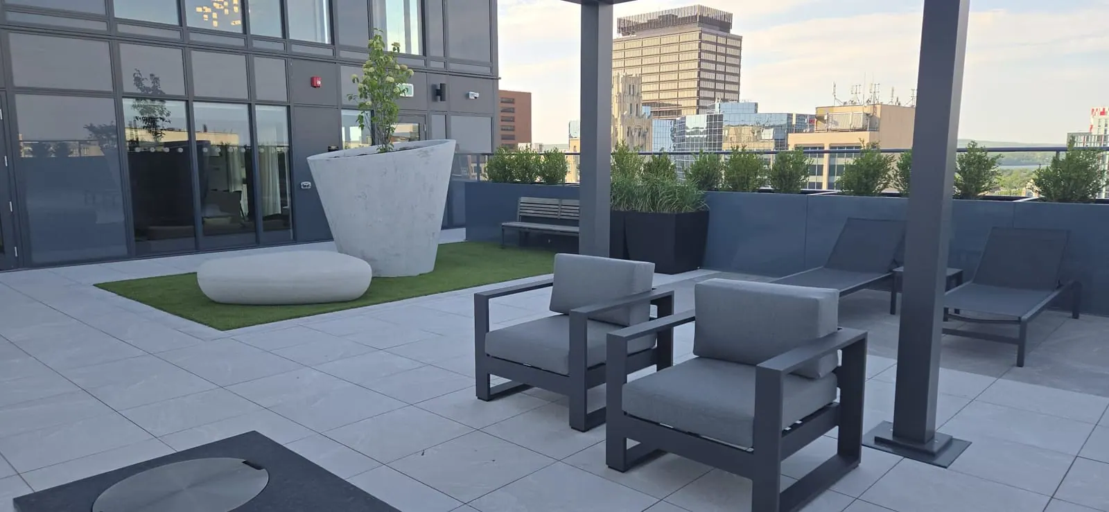 Two modern lounge chairs on the rooftop facing the city skyline under a soft evening sky.