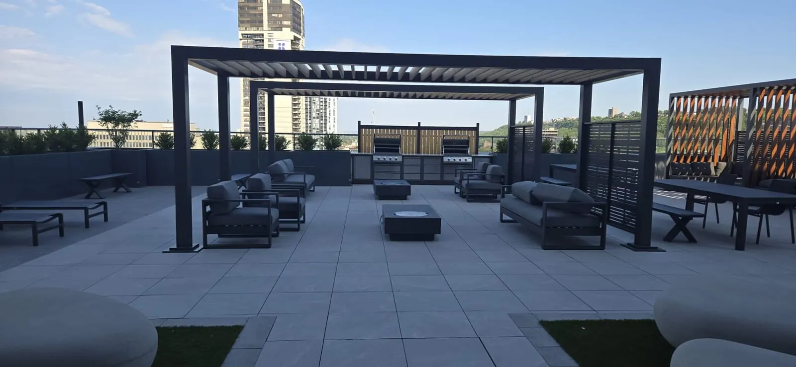Rooftop lounge under a dark pergola with a downtown glass tower framed cleanly against a clear sky.